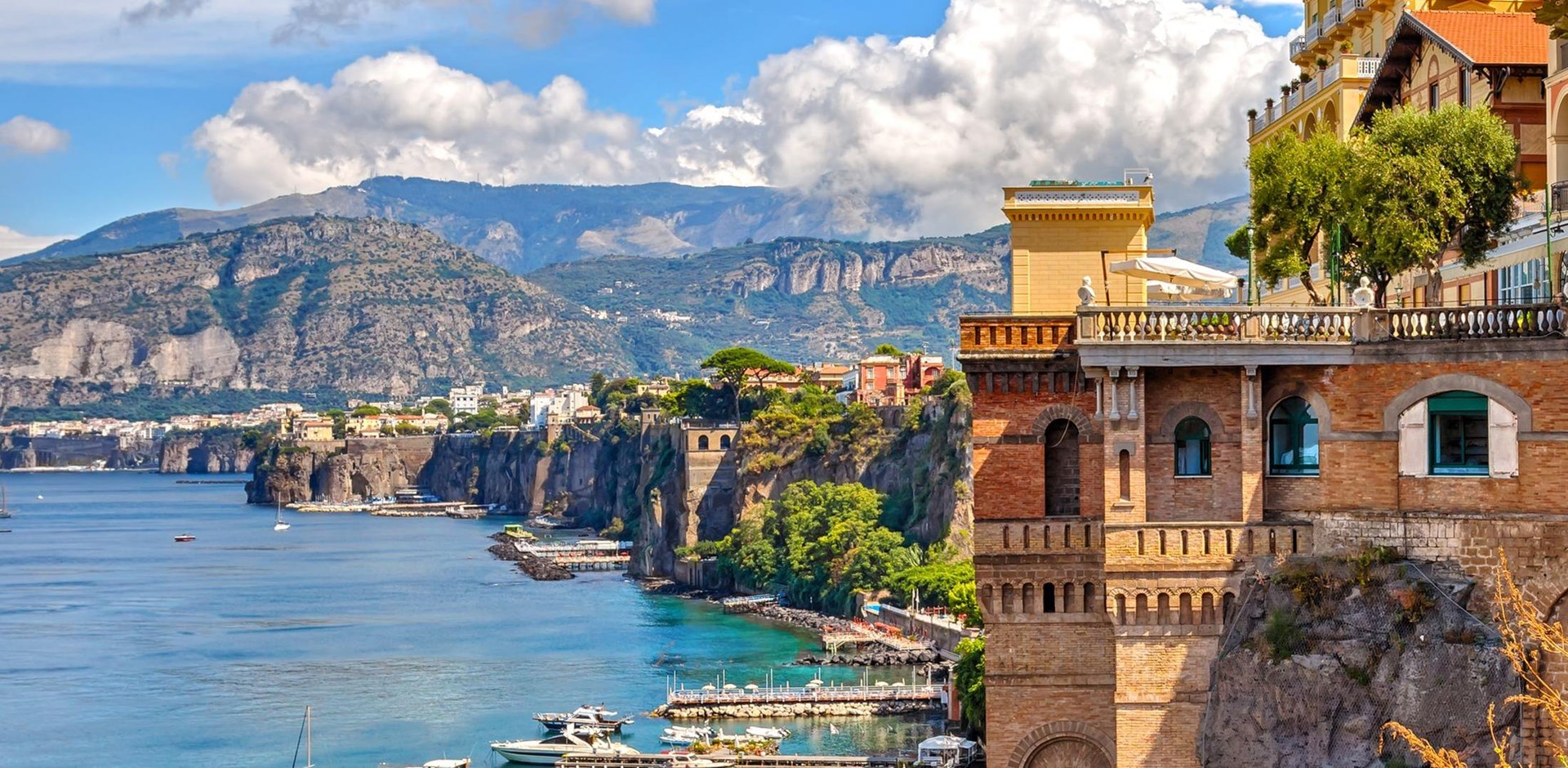 A view of the coast of Sorrento, with a classic building on the right, and mountains in the background