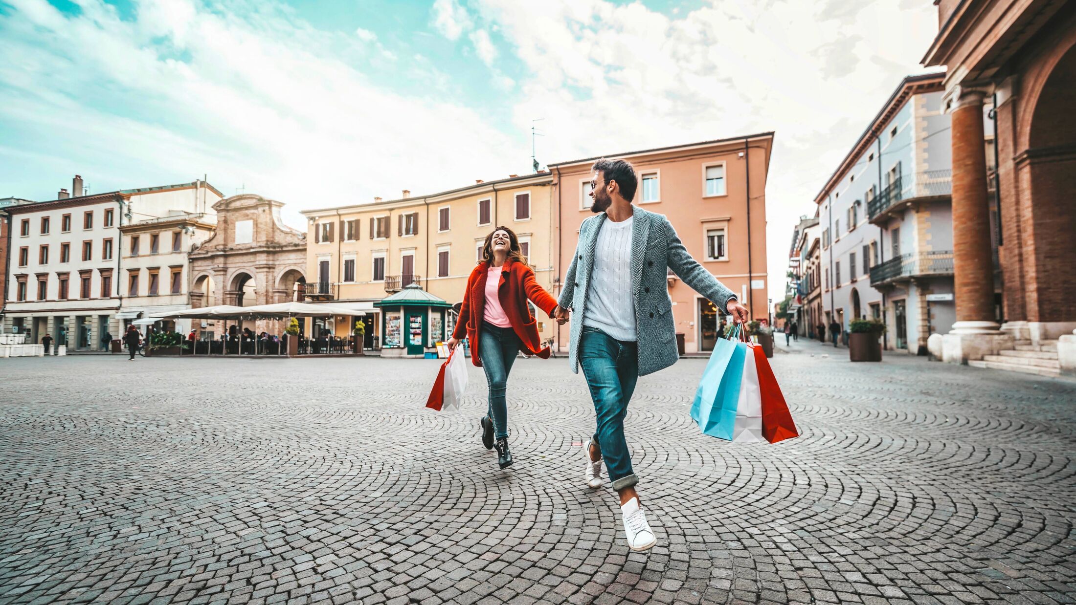 Happy beautiful young couple holding shopping bags walking on city street - Two loving tourists having fun on weekend vacation - Holidays and shopping concept