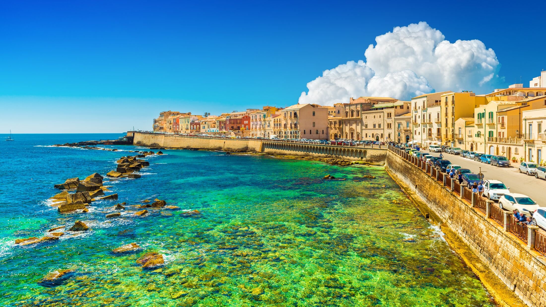 Beautiful cityscape of Ortygia (Ortigia), the historical center of Syracuse, Italy. Skyline of a European coastal town with turquoise transparent water and picturesque clouds in the sky