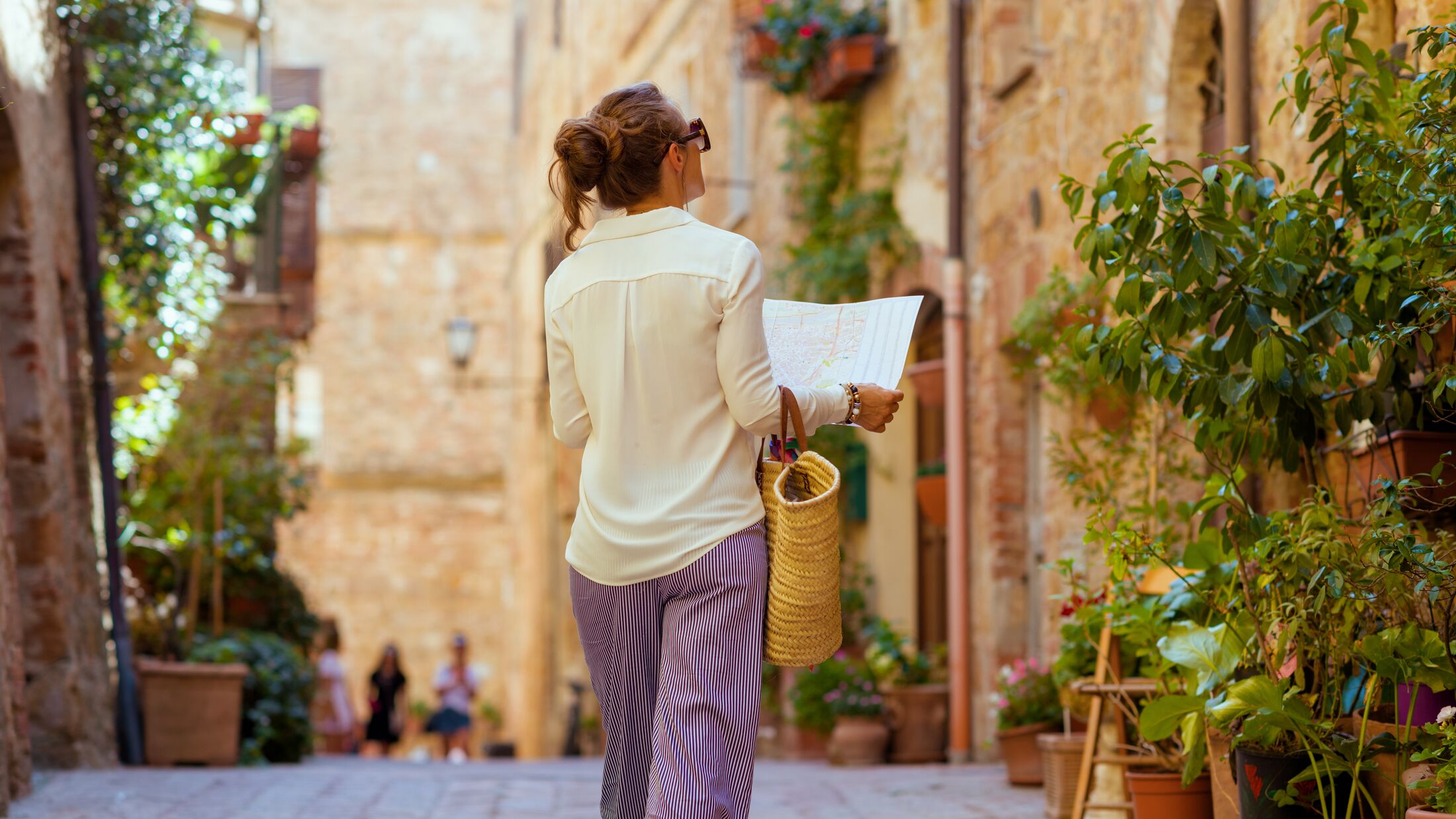 Travel in Italy. Seen from behind elegant solo tourist woman with map and straw bag sightseeing in Tuscany, Italy.