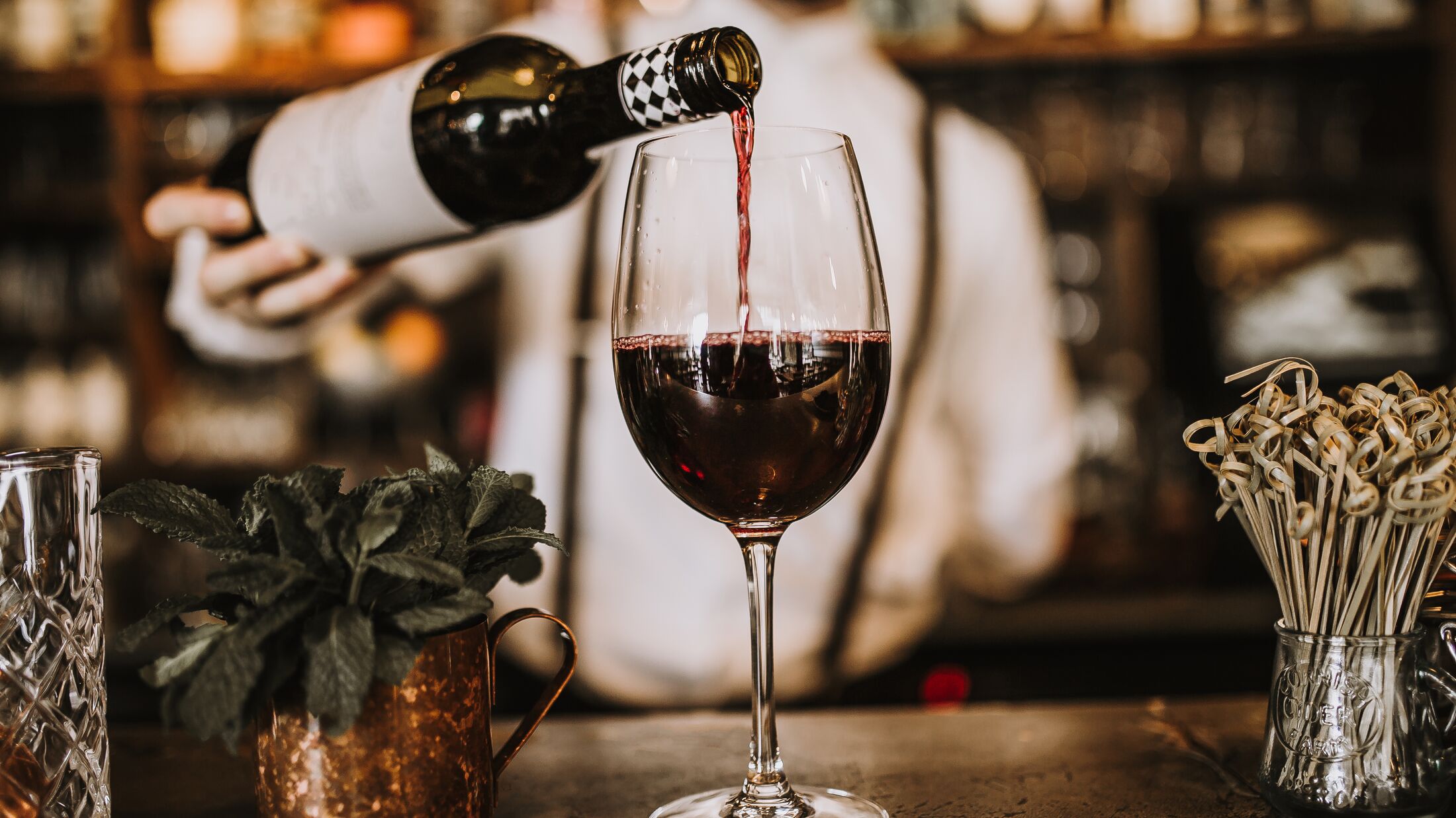 Bartender pouring red wine from a bottle in a wine glass, selective point of view on a wine glass